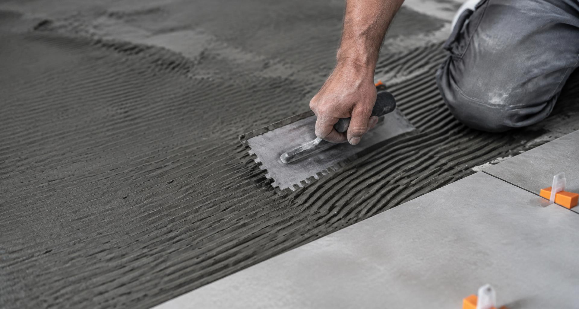 Installer using a notched trowel on gray thinset with orange tile spacers